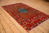 Angled profile of an antique Anatolian rug with its stepped blue medallion and intricate red boteh-filled field.