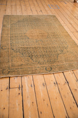 Distressed corner of a vintage Bijar rug, showing faded brown, teal tones, and short fringe.