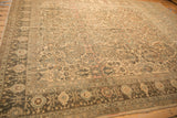 Dark ornate border contrasting the muted, distressed floral field of a vintage Lilihan carpet.