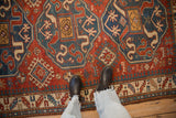 Bold geometric medallions and pawn motifs on an antique Kazak rug shown for scale underfoot.