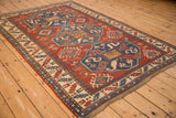 Angled view of an antique Caucasian Kazak rug with bold triple medallions in red, blue, and ivory.