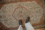 A person's view standing on the antique Malayer rug, showing the texture and terracotta medallion.
