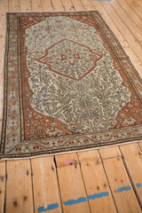 An antique Malayer rug viewed at an angle, showing the terracotta shield medallion and intricate pattern.