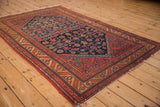 Angled view of a vintage Malayer rug showing its navy Herati field and complex red borders.