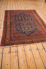 Angled view of a vintage Malayer rug, displaying its navy blue Herati field and intricate red border.