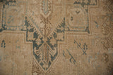 Close-up of distressed Heriz rug with faded sandy brown and dusty teal geometric motifs.