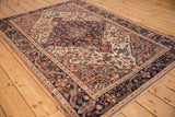 High-angle view of a distressed Malayer rug highlighting its navy blue medallion and ivory floral field.