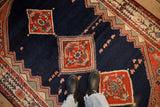 Overhead view of a vintage Malayer rug's red medallions and floral motifs on a navy blue open field.