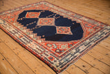 A vintage Persian Malayer rug from an angle, showing its navy field and triple terracotta medallions.