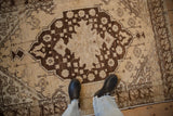 Vintage distressed Oushak rug, cream field, dark brown shield medallion, and heavy abrashes.