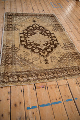 Distressed Oushak rug corner with a faded dark brown and cream tulip border pattern.