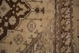 Distressed Oushak rug with dark brown geometric and tulip patterns, heavy abrashes, and side selvage.