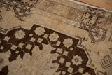 Distressed Oushak rug detail: dark brown geometric florals on faded cream, visible abrash.