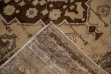 Distressed Oushak rug corner showing worn dark brown and beige pile with woven foundation.