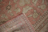 Flipped corner of a vintage Oushak carpet showing its hand-knotted weave and dusty rose pile.