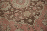 Angled view of the distressed Oushak pile showing floral motifs in dusty rose and coffee brown.