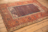 Close detail of antique Malayer rug corner with navy field, allover boteh, and brick red border.