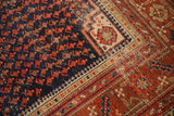 Corner detail of an Antique Malayer rug with navy field, red boteh motifs, and areas of foundation showing.
