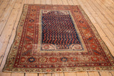 Hand-knotted antique Malayer rug corner: navy boteh field, brick red border, visible wear.