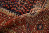 Antique Malayer rug's folded view: navy boteh patterns, brick red border, hand-knotted texture.