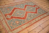 Angled view of a distressed vintage rug's stepped red medallion and dusty blue geometric field.