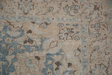 The distressed texture of a vintage Tabriz carpet showing worn floral patterns in dusty blue.