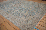 Angled view of a distressed Tabriz carpet showing its low pile and soft dusty blue and ivory floral pattern.