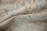 The worn, hand-knotted texture of a distressed Persian rug in beige with blue accents.