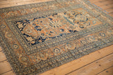 Angled view of an antique Tabriz rug showcasing its sandalwood field and intricate navy blue borders.