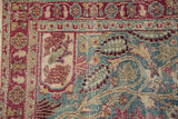 The worn, hand-knotted pile and floral border of a vintage Persian Meshed rug.