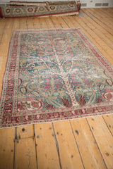 An angled view of the distressed Persian rug showing its full Tree of Life pattern and time-softened colors.