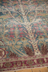 Detailed view of the Tree of Life's delicate vines and red blossoms on a vintage distressed rug.