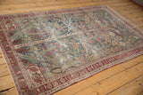 Angled view of a vintage Meshed rug with decorative wear over its blue and red Tree of Life design.