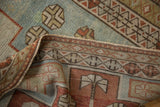 Folded corner of a vintage Caucasian rug displaying the low-pile texture and geometric border.