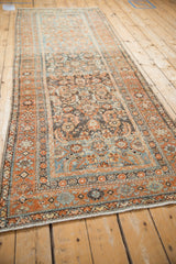A long, angled view of the distressed vintage Malayer runner's allover Herati design.