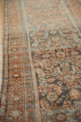 Angled side view of a vintage Malayer runner's rust border and worn blue Herati field.