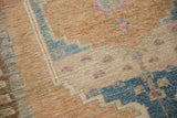 Distressed hand-knotted texture showing sand, pale blue, and magenta geometric motifs.