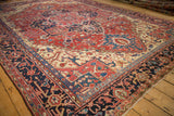 Angled view across a vintage Heriz carpet showing the detailed navy border and geometric red field.