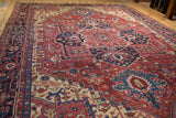 Low angle view of the rich texture and geometric patterns on a vintage red and navy Heriz carpet.