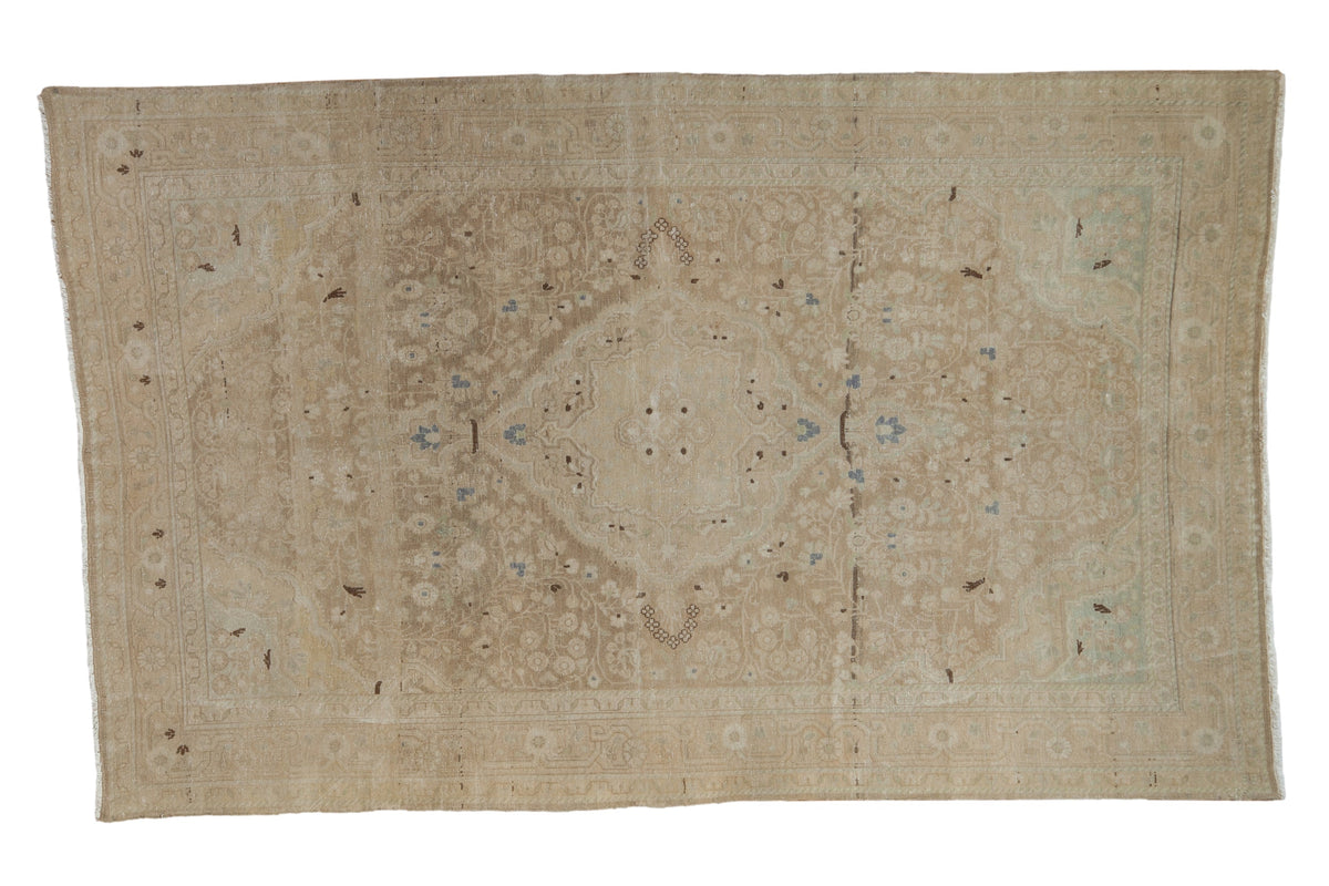 Distressed vintage Sarouk rug with a central medallion, scrolling vines, and soft beige and brown tones.