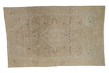 Distressed vintage Sarouk rug with a central medallion, scrolling vines, and soft beige and brown tones.