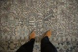 Close view of a distressed vintage Heriz rug showing geometric arabesques in slate blue and charcoal on a beige field.