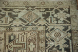 Geometric turtle samovar border detail on a distressed Heriz carpet in beige and charcoal.