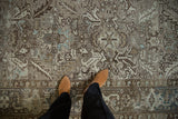 Close-up showing the low pile, floral vines, and turtle motifs of a distressed Persian Heriz carpet.