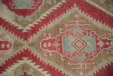 Serrated medallion detail in raspberry red, seafoam, and dusty bronze on a distressed rug.