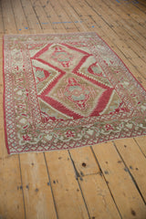 Angled view of a vintage distressed Caucasian rug showing its raspberry red serrated medallions.