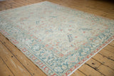 Angled view of a vintage Heriz carpet showcasing its traditional design in muted ivory, teal, and red.