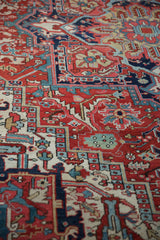 Intricate patterns of a Heriz carpet, showcasing rich cherry red, navy, and teal hues.