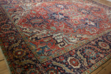 Vintage Heriz carpet showing intricate serrated leaf, floral, and vine patterns on cherry red and navy.
