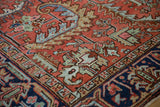 Close-up of a traditional Persian Heriz carpet's madder red field with colorful serrated leaves and navy border.